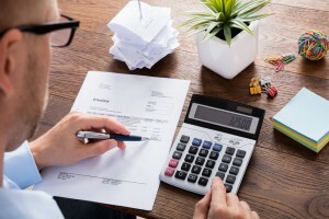 Redução de custos nas empresas: estratégias de sucesso e tendências (Foto: homem usando a calculadora e anotando no papel)