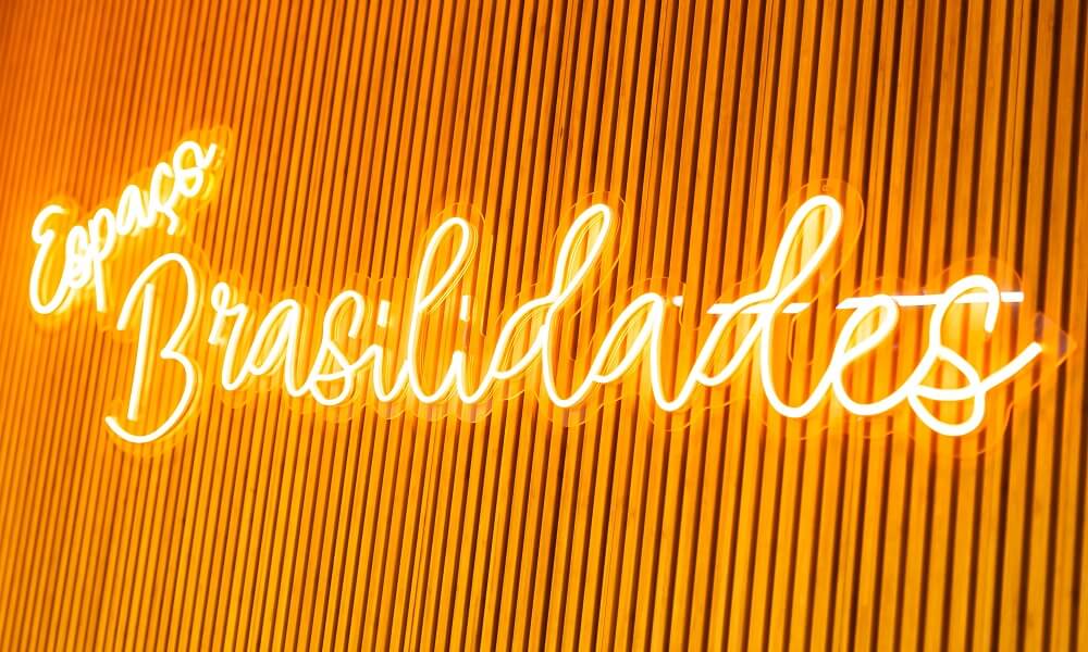 #pracegover: Letreiro na Copastur, de cor laranja, iluminado em parede de madeira, diz "Espaço Brasilidades"