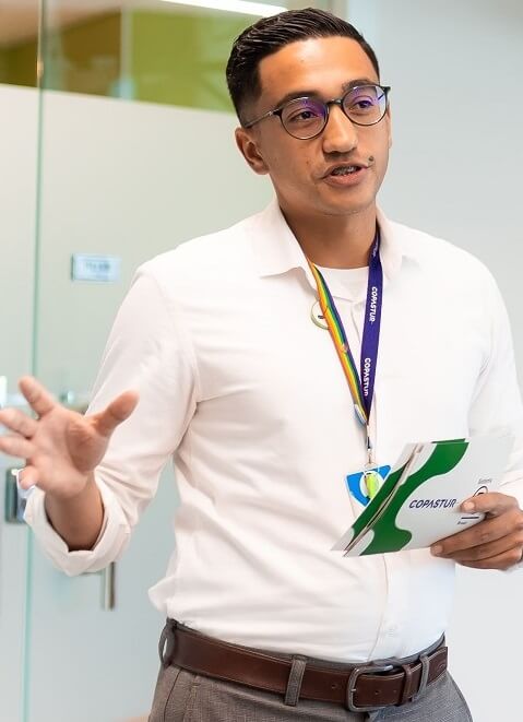 Maurício Santos - Gerente de Sucesso do Cliente na Copastur - Café B (#pracegover: Homem com cabelos curtos e escuros, vestindo camisa social branca, com crachá com cores do arco-íris, segura ficha de palco com logotipo da Copastur e do Sistema B)