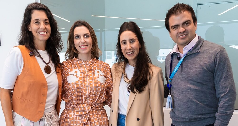 Painelistas do Café B na Copastur - Cinthia, Letícia, Helena e Edmar (#pracegover: da esquerda para a direita, três mulheres e um homem reunidos, sorrindo e olhando para a câmera; a primeira tem cabelos longos e ondulados escuros e usa blusa branca com colete laranja e colar marrom, a segunda tem cabelos curtos e lisos com reflexos loiros e usa camisa de botões xadrez alaranjada, a terceira tem cabelos escuros, lisos e longos e usa blusa branca com casaco bege e colar bege, e o quarto tem cabelos curtos e escuros e usa blusa social branca com blusa cinza de manga comprida por cima e crachá azul) 