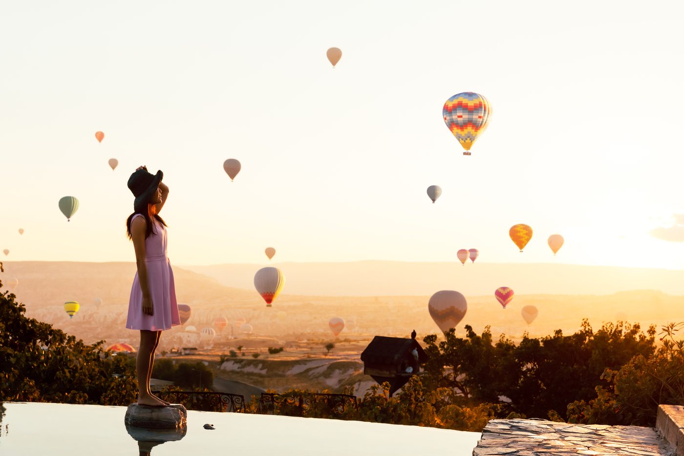 Viajera en la terraza de un hotel con piscina, frente a los globos de Capadocia al amanecer